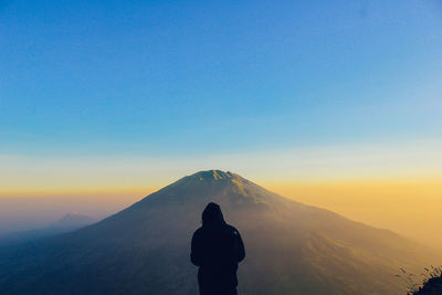 Rear view of silhouette man standing on mountain against sky