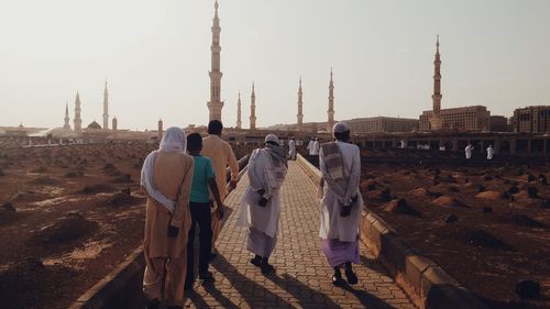 Rear view of people walking on footpath by cemeteries against clear sky