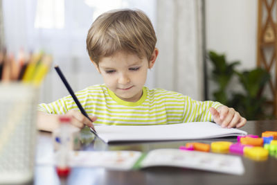 Boy drawing on book at table