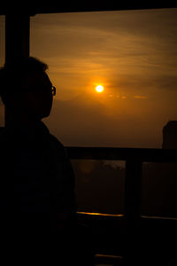 Silhouette man by sea against sky during sunset