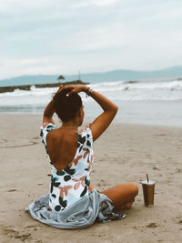 Rear view of woman sitting at beach against sky