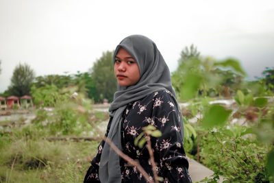 Portrait of young woman standing on field against sky