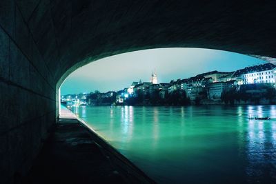 Arch bridge over river in city against sky at dusk