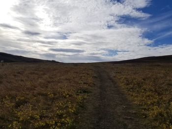 Dirt road amidst field against sky