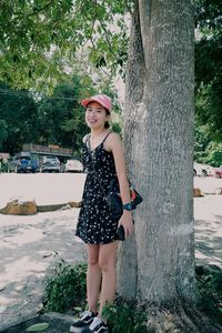 Portrait of beautiful young woman standing against tree trunk
