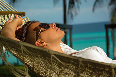 Side view of woman lying in hammock at beach