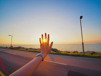 Cropped image of woman hand against sea and sky during sunset