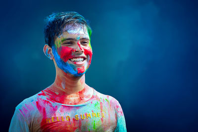 Happy young boy with face covered in colors against blue background