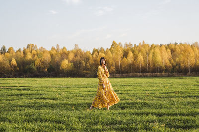 Woman wearing yellow dress standing in autumn field on sunny day