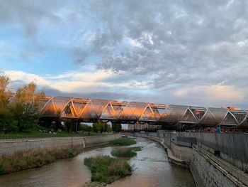Bridge over river by buildings against sky