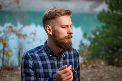 Smoking bearded man outdoors near lake in the evening. bad habit, addiction