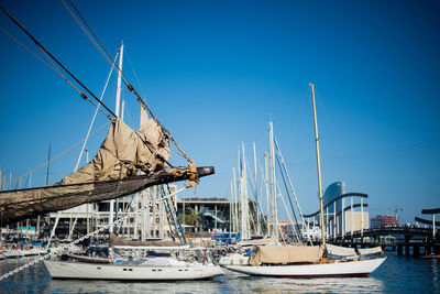 Sailboats moored at harbor against clear blue sky