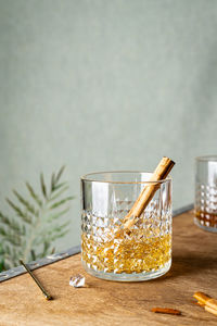 Crystal glass with whiskey served with stick of spicy cinnamon placed near leaf on corner of table