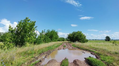 Country road with puddle after rain on background of blue sky with clouds