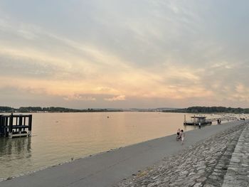 People on pier at beach against sky during sunset