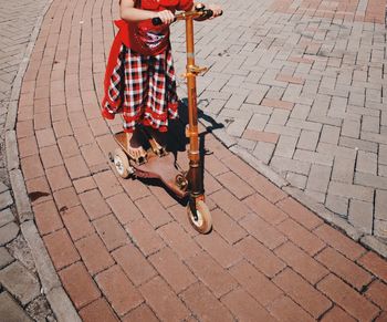 Low section of girl riding push scooter on cobbled street