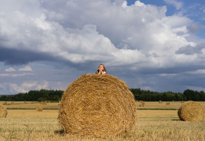 Little girl on the stack hay on summer field.