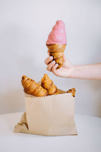 Close-up of hand holding ice cream cone against white background