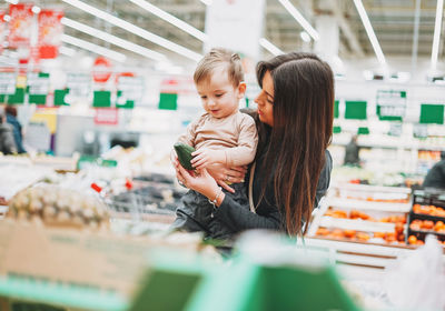 Woman showing avocado to son while shopping at supermarket