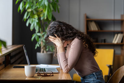 Exhausted unhappy woman sit at laptop hide face in hands tired work overtime suffer from burnout