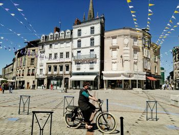 Woman cycling on street against buildings in city