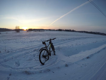 Bicycle on snow covered field against sky during sunset