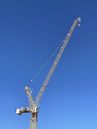 Low angle view of crane against clear blue sky