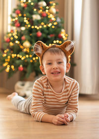 Portrait of cute boy lying on floor against christmas tree at home