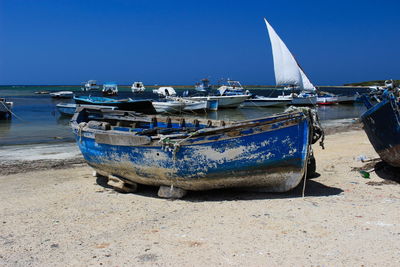 Boats moored on beach against clear blue sky