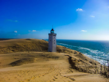 Lighthouse on beach by sea against sky
