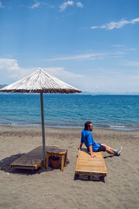 Man in a blue shirt sitting on a sunbed by the beach under an umbrella on the sea