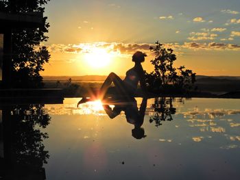 Silhouette people by lake against sky during sunset