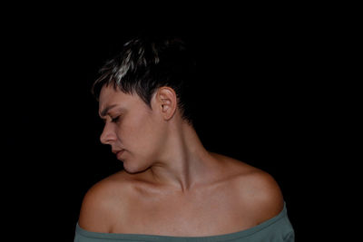 Close-up of shirtless young woman against black background