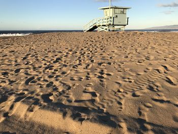 Footprints on sand at beach against sky with lifeguard house backdrop 
