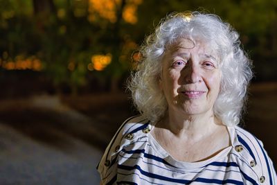 Portrait of an elderly smiling grey-haired curly woman with long hair on the street of a night city.