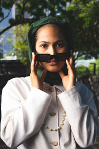 Portrait of a beautiful young woman holding sunglasses outdoors