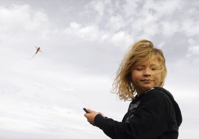 Low angle view of boy flying kate against sky