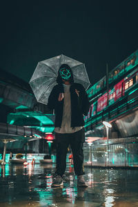 Low angle view of man wearing mask with umbrella standing on footpath