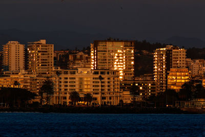 Illuminated cityscape by sea against sky at night