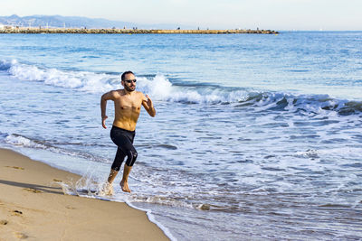 Shirtless man running on shore at beach