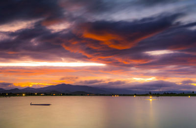 Scenic view of lake against dramatic sky during sunset