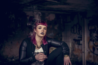 Portrait of young woman smoking cigarette in abandoned building