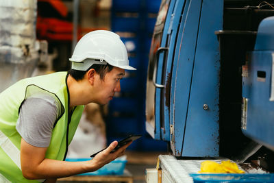 Side view of man holding digital tablet by machinery in factory