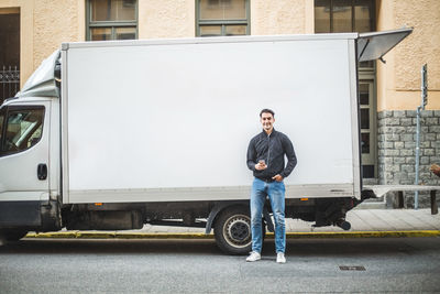 Portrait of male mover standing against truck on street in city