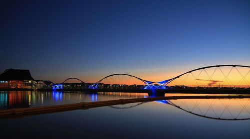 Arch bridge over calm river against clear sky during sunset