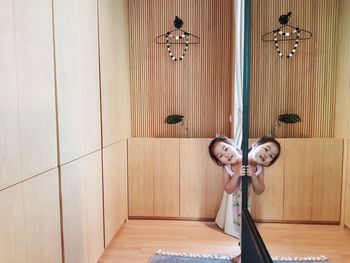 Girl peeking through wall with reflection in mirror at home