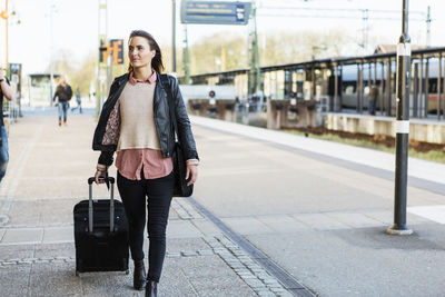 Businesswoman pulling wheeled luggage while walking on railroad station platform