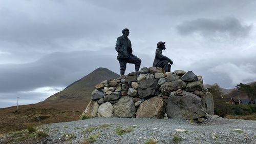 Low angle view of statue of men on rock against sky