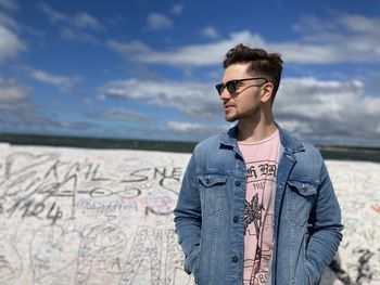 Young man wearing sunglasses standing against sky