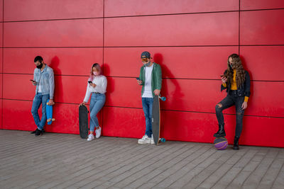 Full length of people wearing mask standing against red wall